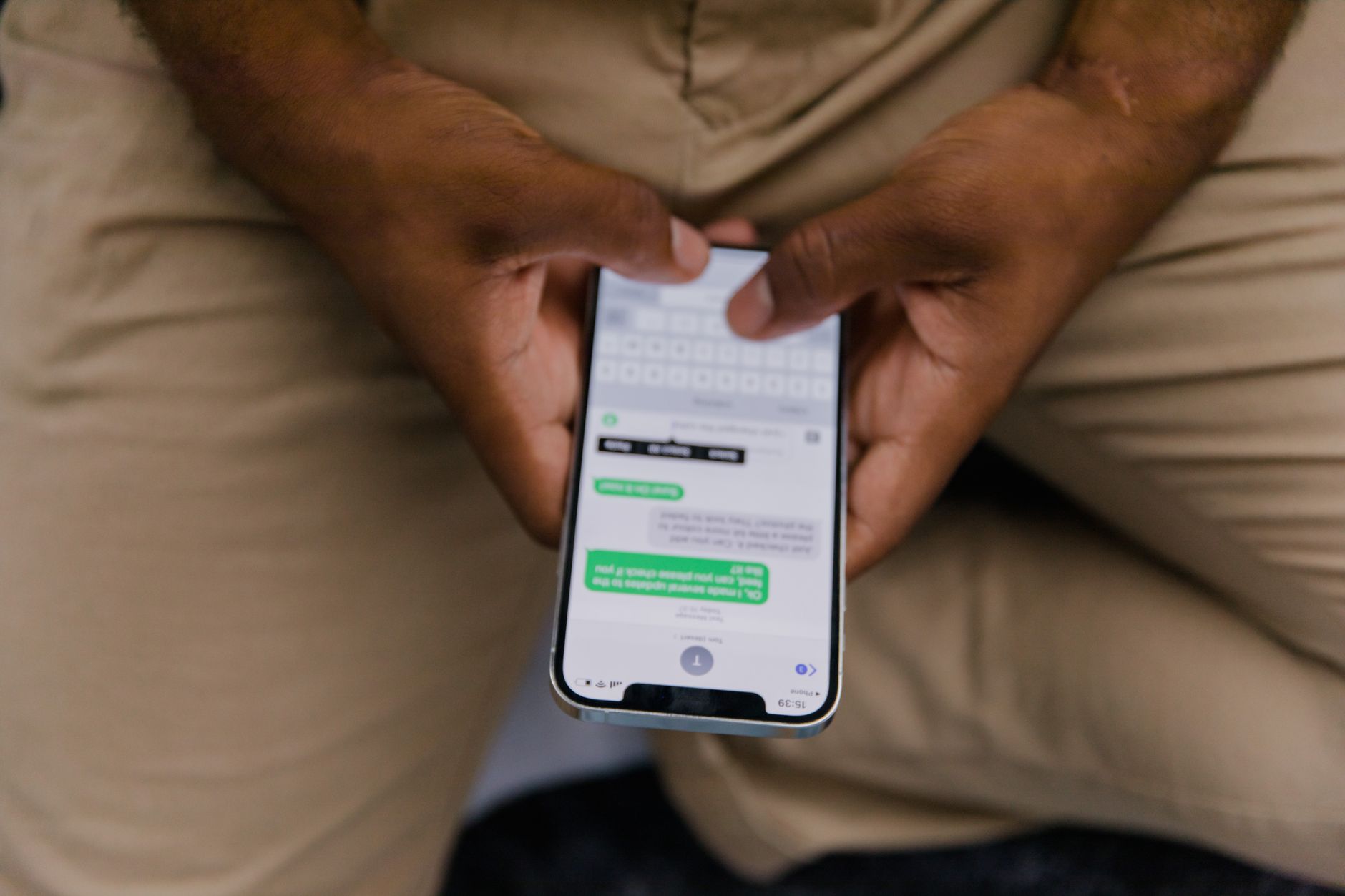 A person's hand holding a smartphone and taking a screenshot of a messaging conversation, with a notebook and pen on a table nearby.