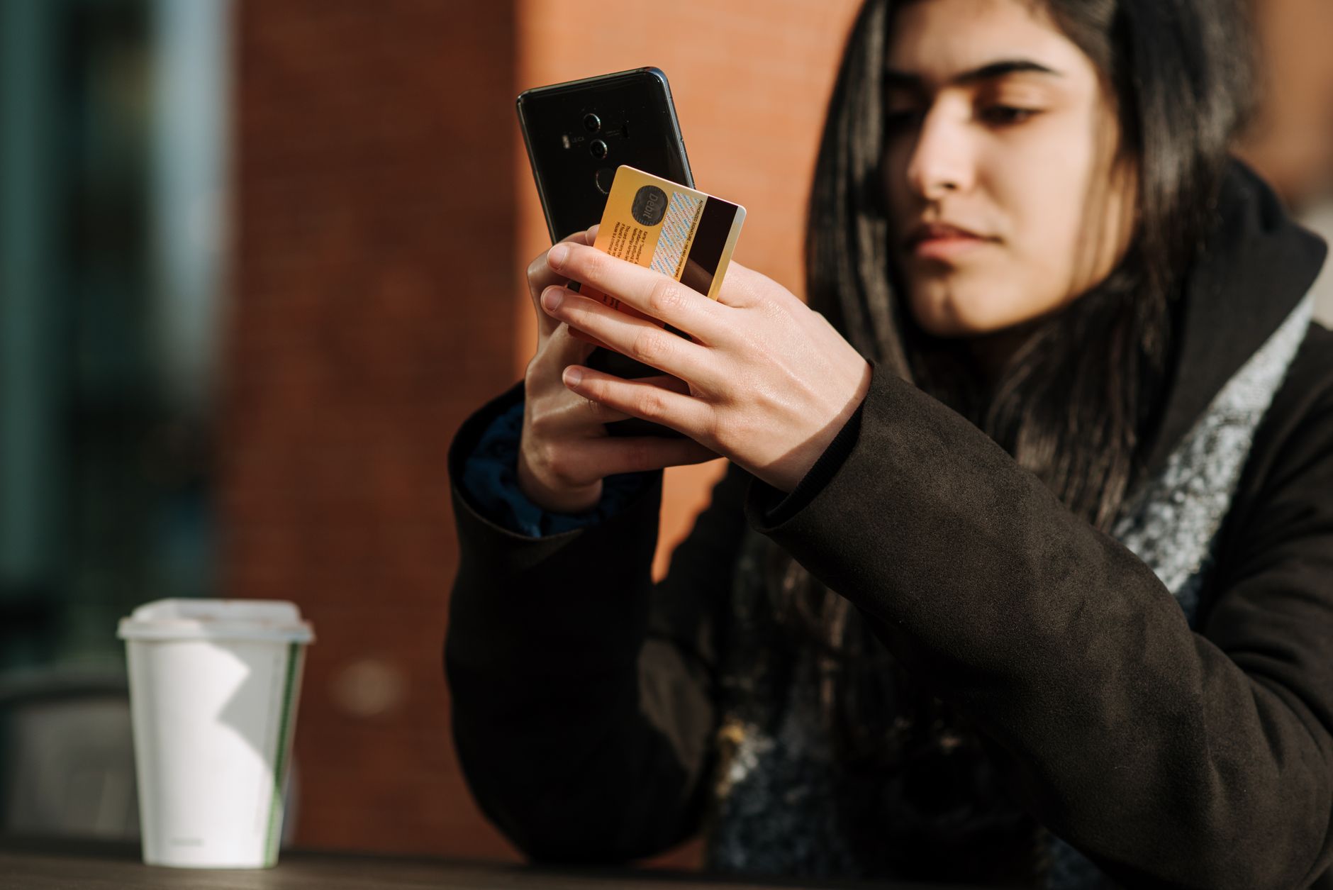 A worried person looks at a smartphone while a credit card and gift card sit on a table, showing a suspicious online money request.