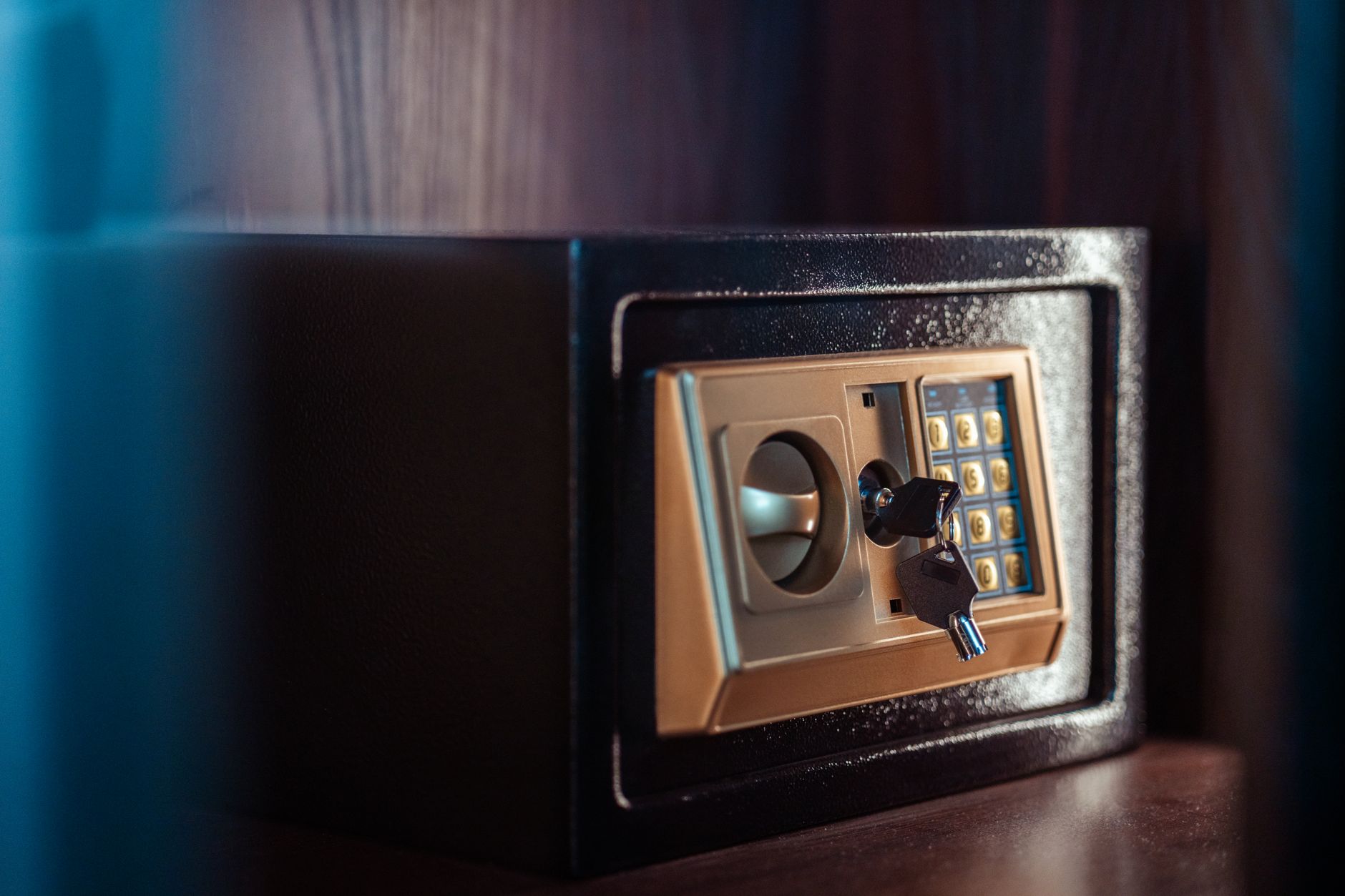A hand places a folded paper into a small locked safe on a desk, showing secure document storage.