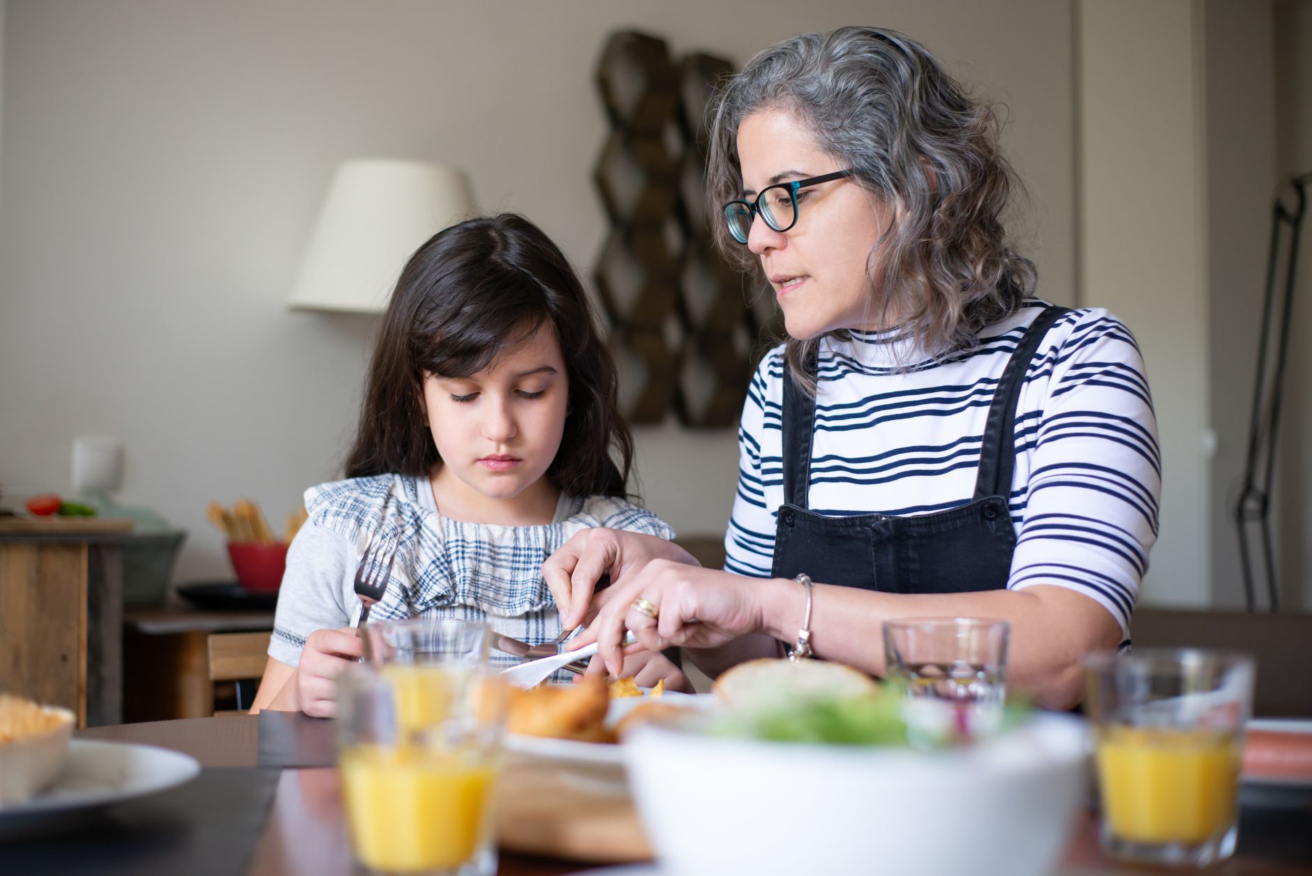 An adult child gently holding hands with an elderly parent while talking at a kitchen table.