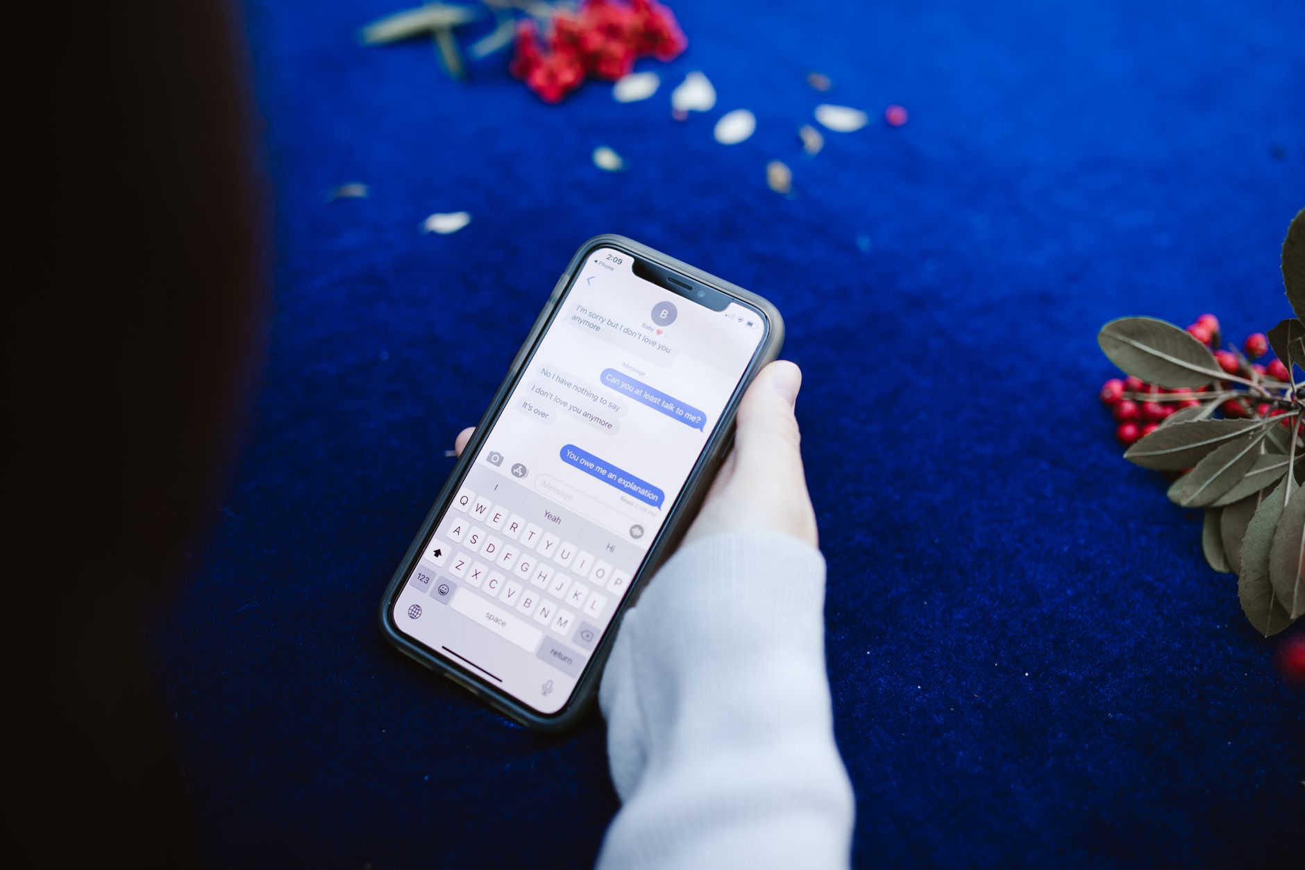 A person holds a smartphone and takes a screenshot of a suspicious text message while sitting at a desk.
