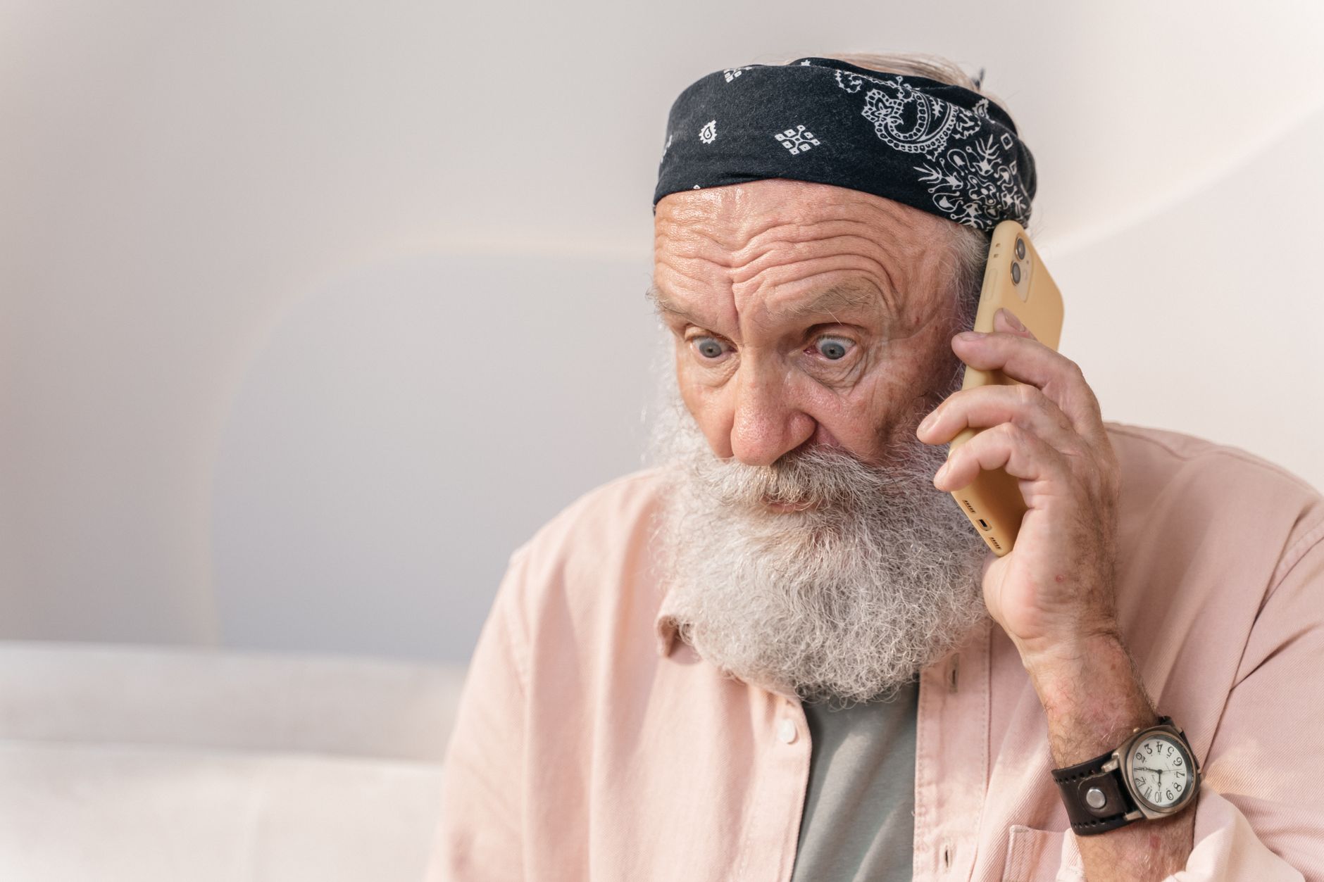 An older man at a kitchen table looks at his phone with a suspicious, concerned expression